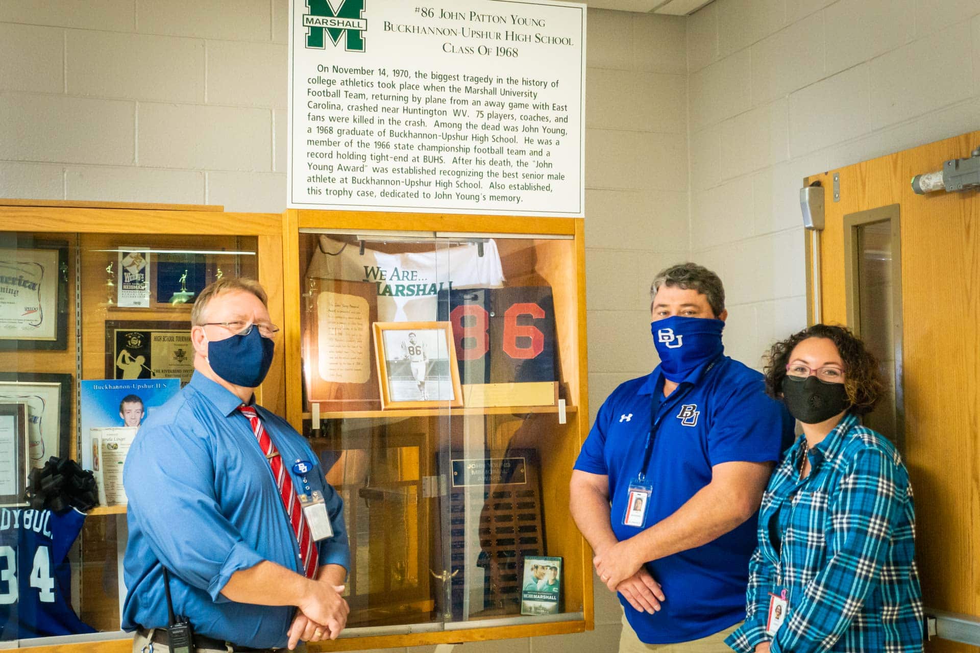Buckhannon-Upshur High School assistant principals Randall Roy and Samantha LePut join athletic director Rick Reynolds (center) in front of the display case for the John Young Award, which is given to the top senior male athlete each year.