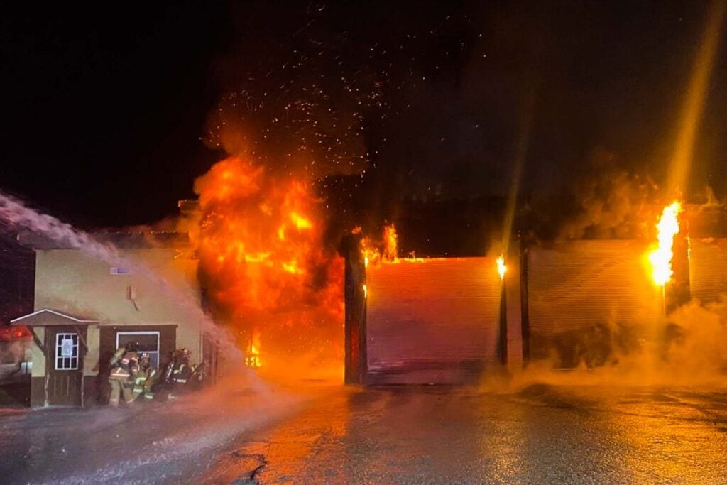 Firefighters huddle behind cover as a large blaze consumes a WVDOH maintenance garage near Coalton on Monday. (Photo courtesy WVDOH)