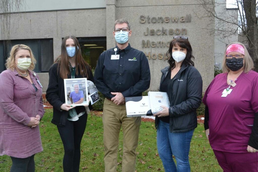 Members of the Mon Health Stonewall Jackson Memorial Hospital (SJMH) administration accept a donation of an iPad and Android tablet to be used by COVID patients at the Weston hospital. The donation is in memory of the Buckhannon family's patriarch Tex Walton. Pictured left to right are Chief Nursing Officer Carole Norton, Walton's granddaughter NinaMae Coberly, SJMH Chief Operating Officer Kevin Stalnaker, Walton's daughter Sheila Perry, and SJMH Nurse Manager Carla Hamner.