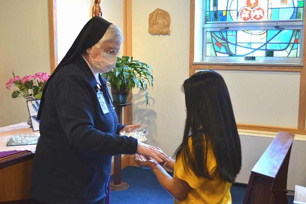 Sister Francesca Lowis, SAC, offers a blessing of the hands Friday to Ariana Long, who will be traveling with the Hands and Hearts for Christ to Guatemala in 2022 on a mission trip.