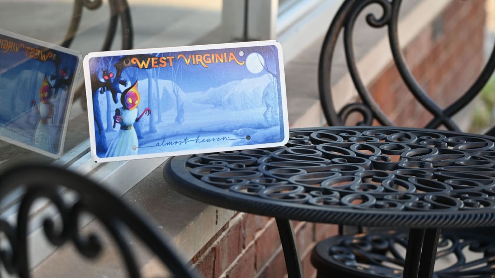 The cryptids license plate rests in a window beside a metal table.